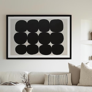 May include: A framed abstract art print featuring a grid of twelve black, rounded shapes on a light gray background. The artwork is displayed in a black frame and hangs above a white sofa with decorative pillows.