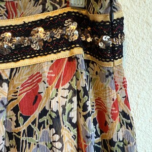 May include: A colorful skirt with a floral pattern in red, green, and yellow. The skirt has a black sequined band with gold trim at the waist. The fabric appears to be lightweight and flowing.