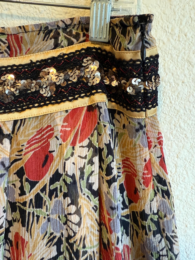 May include: A colorful skirt with a floral pattern in red, green, and yellow. The skirt has a black sequined band with gold trim at the waist. The fabric appears to be lightweight and flowing.