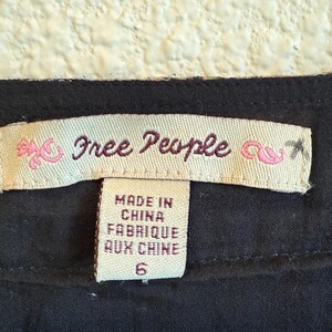 May include: Close-up of a clothing label with the brand name "Free People" in cursive script. The label also states "Made in China Fabrique aux Chine" and the size "6". The label is on a black fabric.