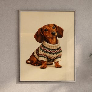Dachshund sweater wall art print featuring a warm chestnut brown dachshund in a cream knit sweater with festive green and rust-red patterns, set against a soft beige background, framed and leaning against a beige sofa on a textured rug in a bright Scandinavian living room.