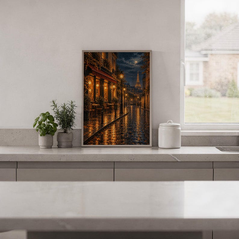 Paris eiffel tower wall art print standing on a white kitchen counter beside potted herbs.