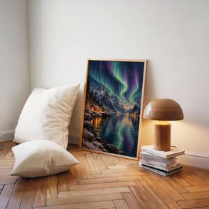 Aurora borealis mountain landscape wall art print leaning on a herringbone wood floor beside cream cushions and a wooden mushroom lamp.