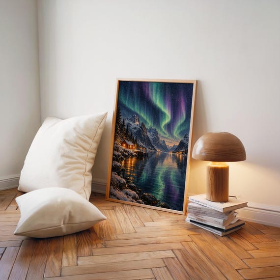 Aurora borealis mountain landscape wall art print leaning on a herringbone wood floor beside cream cushions and a wooden mushroom lamp.