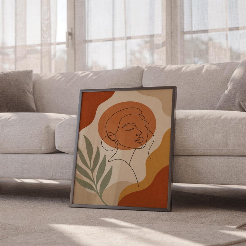 Abstract line art face print leaning against a white sofa in a bright living room with sheer curtains.