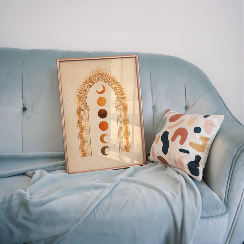 Mid-century boho art poster with celestial sun and moon phases leaning against a light blue sofa with decorative pillow⁠
