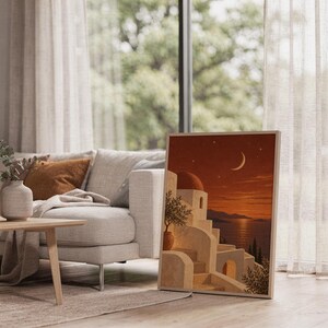 Mediterranean moonlit coastal wall art print leaning on the floor beside a cream armchair next to large garden windows.