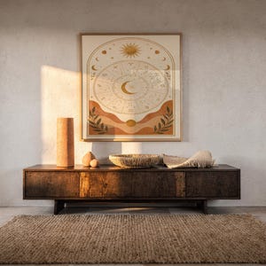 Zodiac wheel wall art print hanging above a dark wood console and jute rug in a warm neutral interior.