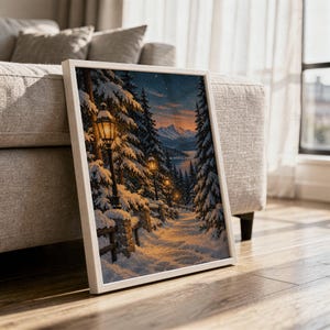 Snowy forest path wall art print in a white frame leaning against a gray sofa on a sunlit wooden floor.