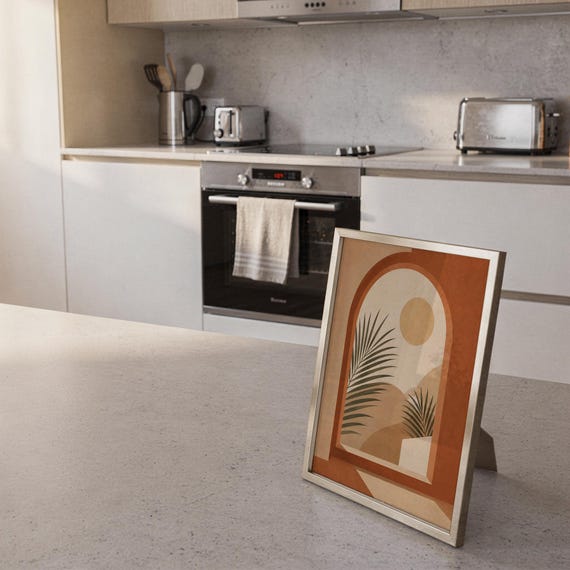 Mid century botanical palm poster framed leaning on bright kitchen island counter in modern home.