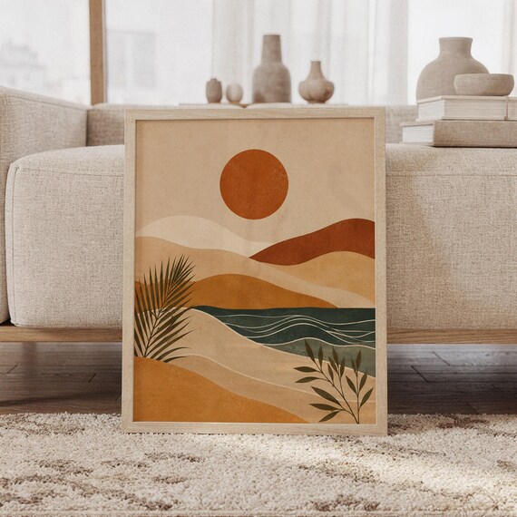 Framed boho abstract desert landscape art print leaning against beige sofa in living room with a sun.