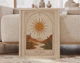 以下が含まれることがあります： 「The Sun」と題されたタロットカードのデザインが描かれた、額縁入りの長方形のウォールアートプリント。中央に光を放つ大きな太陽、ローマ数字のXIX、曲がりくねった川、なだらかな丘、そして金と緑の色合いの植物が描かれています。