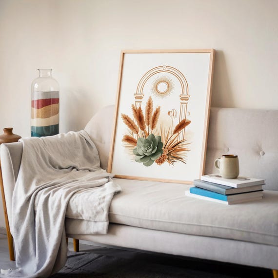 Boho arch wall art poster leaning on a light gray sofa backrest with a soft draped blanket, books on a side table, and minimalist wall decor in a modern cozy apartment living room.