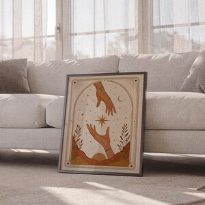 Boho magic hands poster framed leaning against sofa in cozy sunlit living room setup.