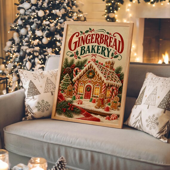 Gingerbread bakery christmas wall art print in a white frame leaning against a gray sofa on a sunlit wooden floor.