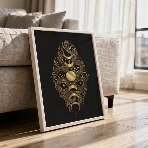 Gold snake moon phase wall art print in a white frame leaning against a gray sofa on a sunlit wooden floor.