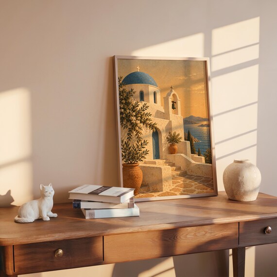 Santorini church wall art print leaning on a wooden desk against a warm beige wall in soft window sunlight.