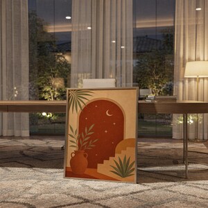 Terracotta moon and stars arch art print standing on a wooden desk in a home office in warm evening light.