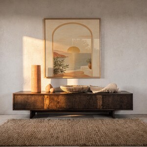 Mediterranean sunset arch print hanging above a dark wood console and jute rug in a warm neutral interior.