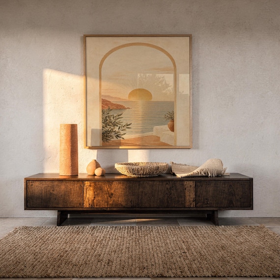 Mediterranean sunset arch print hanging above a dark wood console and jute rug in a warm neutral interior.