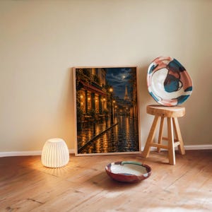 Paris eiffel tower wall art print leaning against a warm beige wall on a wooden floor beside a stool and a glowing lamp.