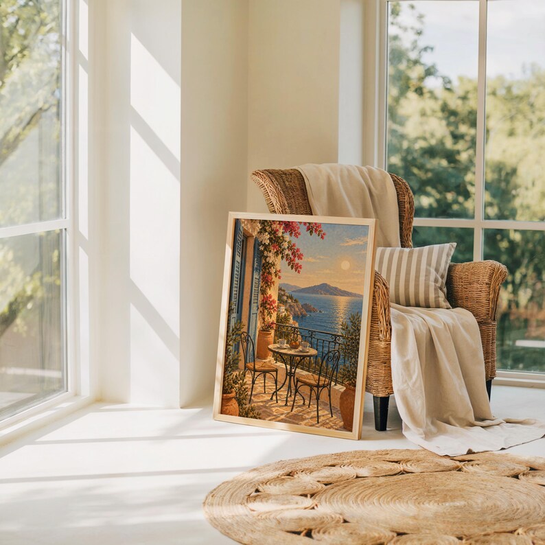Mediterranean balcony wall art print leaning on the floor beside a rattan armchair and jute rug in a bright sunlit room.