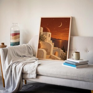 Mediterranean moonlit coastal wall art print leaning on a cream sofa against a beige wall beside books and a mug.