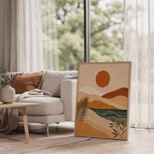 Mid century abstract landscape art poster framed leaning on floor next to white sofa in bright living room.