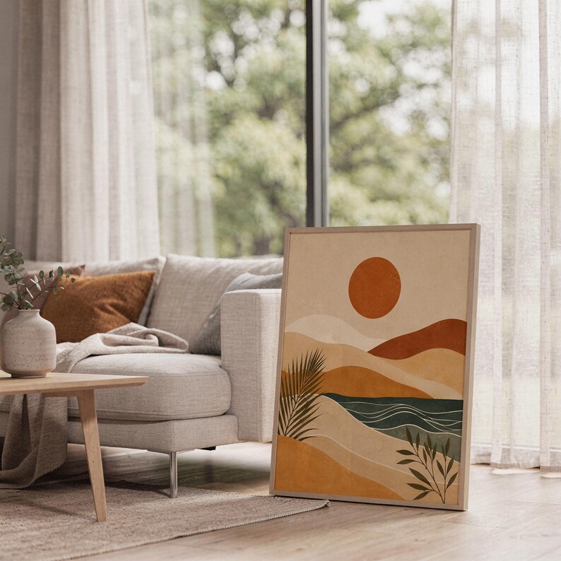 Mid century abstract landscape art poster framed leaning on floor next to white sofa in bright living room.