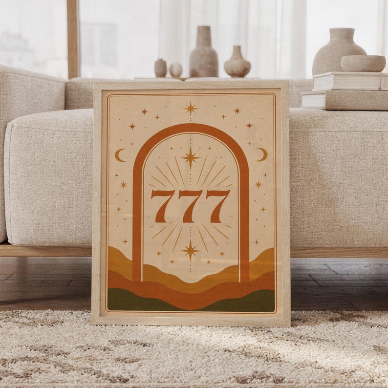 Terracotta 777 angel number wall art print in a wood frame leaning against a cream sofa in a bright modern living room.
