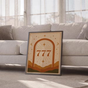 Boho celestial 777 arch poster in a thin frame sitting on the floor in front of a cozy white sofa in a bright living space.