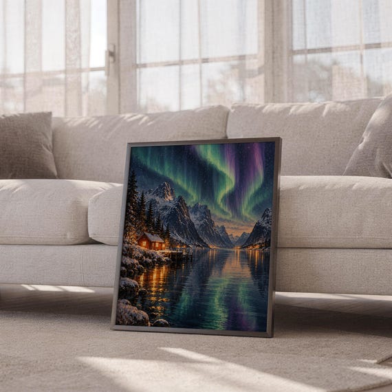 Aurora borealis mountain landscape wall art print leaning against a white sofa in a bright living room with sheer curtains.