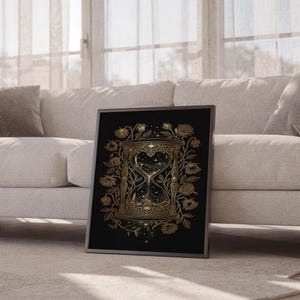 Gothic hourglass wall art print leaning against a white sofa in a bright living room with sheer curtains.