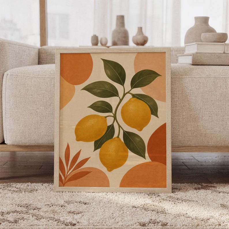 Lemon botanical wall art print of a lemon branch with golden yellow lemons and olive green leaves on a cream background with terracotta shapes, framed and leaning against a beige sofa on a textured rug in a bright Scandinavian living room.