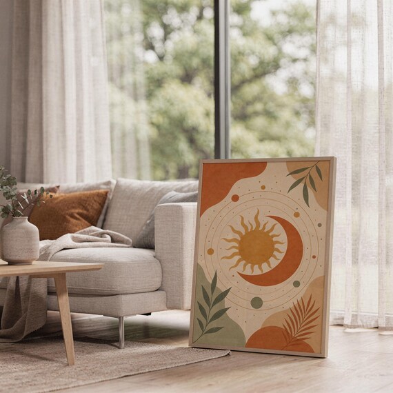 Celestial sun and moon art print leaning on the floor beside a cream armchair next to large garden windows.