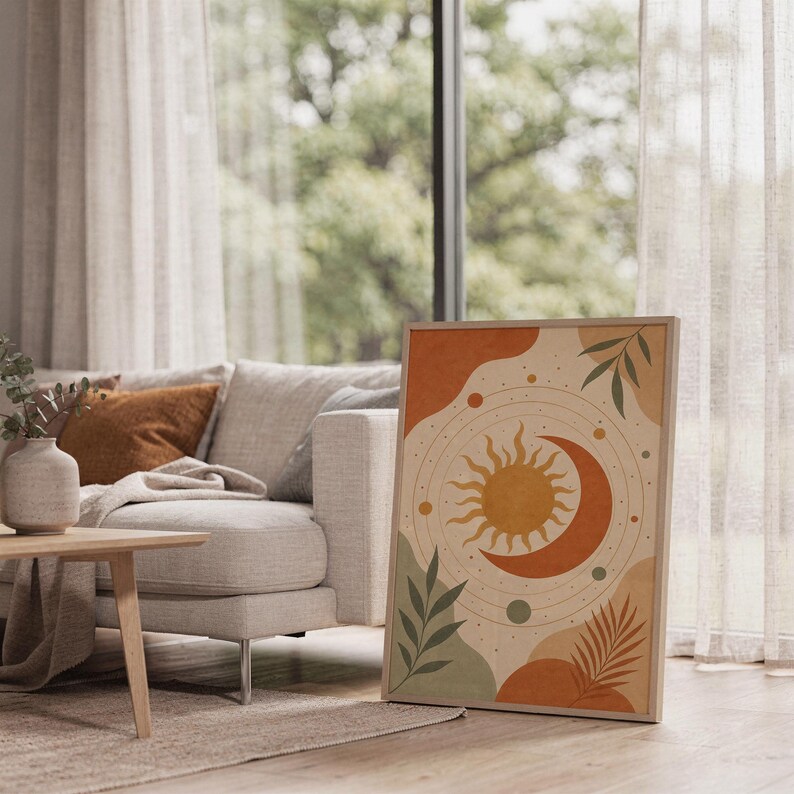Celestial sun and moon art print leaning on the floor beside a cream armchair next to large garden windows.