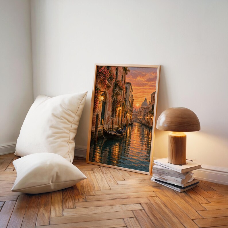 Venice canal sunset wall art print leaning on a herringbone wood floor beside cream cushions and a wooden mushroom lamp.
