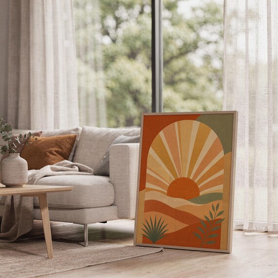Boho sun arch print leaning on the floor beside a cream armchair next to large garden windows.