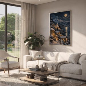 Snowy mountain village wall art print hanging above a white sofa in a living room with garden views.