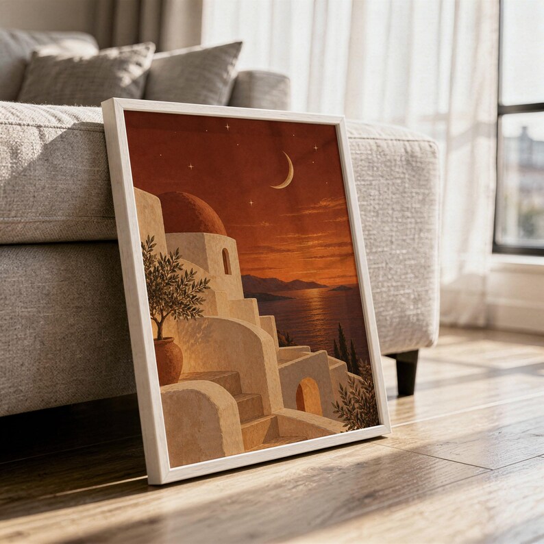 Mediterranean moonlit coastal wall art print in a white frame leaning against a gray sofa on a sunlit wooden floor.