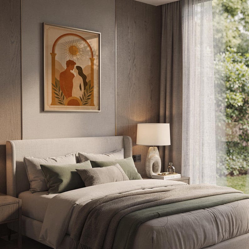 Framed terracotta couple art print hanging above a cozy bed with sage green pillows and neutral bedding in a modern bedroom setting.