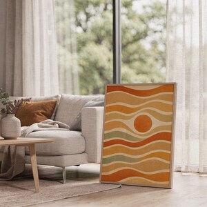 Abstract wavy sun print leaning on the floor beside a cream armchair next to large garden windows.