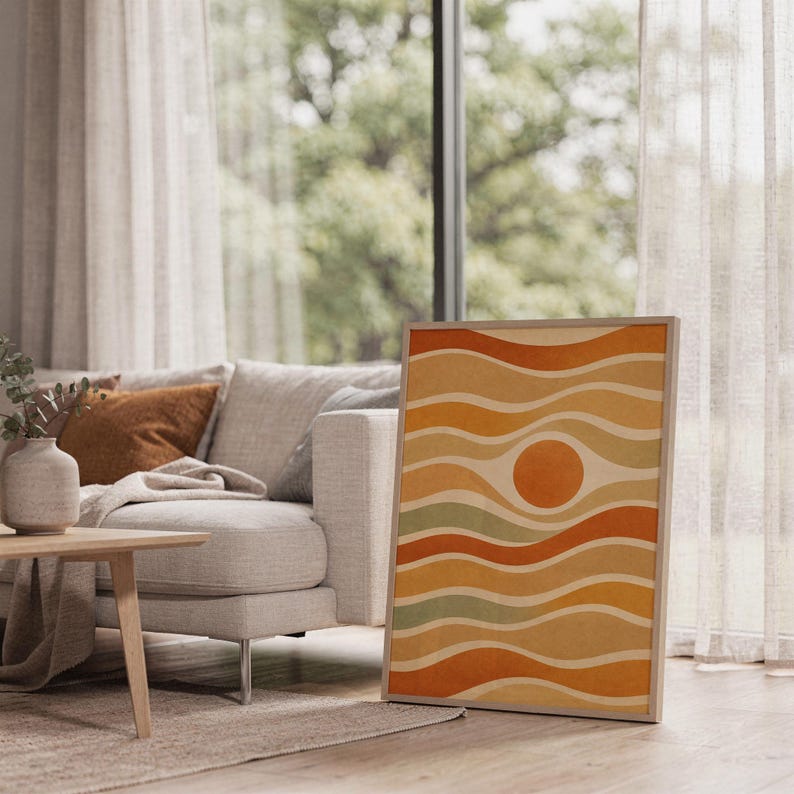 Abstract wavy sun print leaning on the floor beside a cream armchair next to large garden windows.