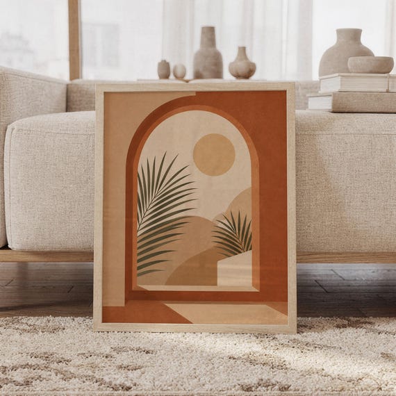 Framed terracotta arch window palm art print leaning on carpet in front of sofa in bright living room.