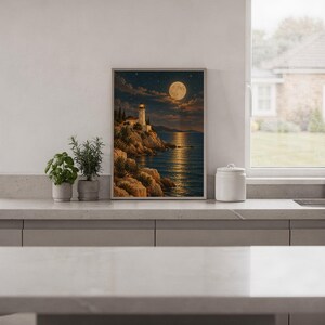 Moonlit lighthouse wall art print standing on a white kitchen counter beside potted herbs.