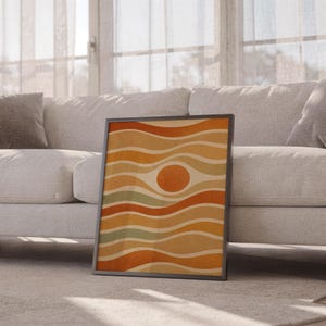 Abstract wavy sun print leaning against a white sofa in a bright living room with sheer curtains.