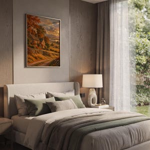 Autumn cottage landscape wall art print leaning on a wooden desk against a warm beige wall in soft window sunlight.