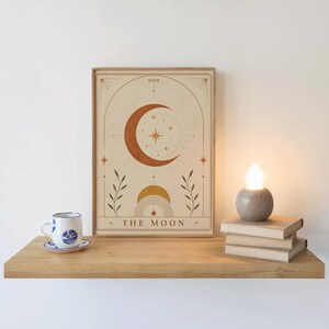 Bohemian moon art print on wooden floating shelf next to coffee cup and candle decor.