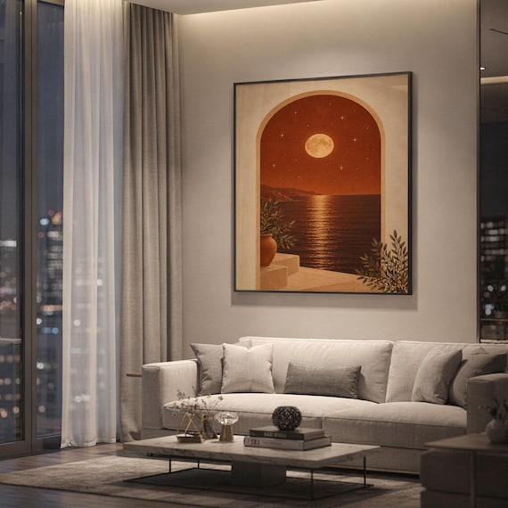 Moonlit Mediterranean arch print showing a glowing full moon and stars over a calm sea and coastal cliffs, framed by an arch with potted plants in terracotta, cream and olive tones, hanging above a light gray sofa in a modern living room with evening city views through tall windows.