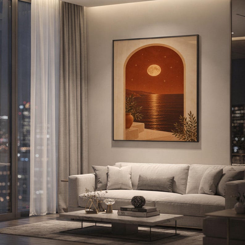 Moonlit Mediterranean arch print showing a glowing full moon and stars over a calm sea and coastal cliffs, framed by an arch with potted plants in terracotta, cream and olive tones, hanging above a light gray sofa in a modern living room with evening city views through tall windows.
